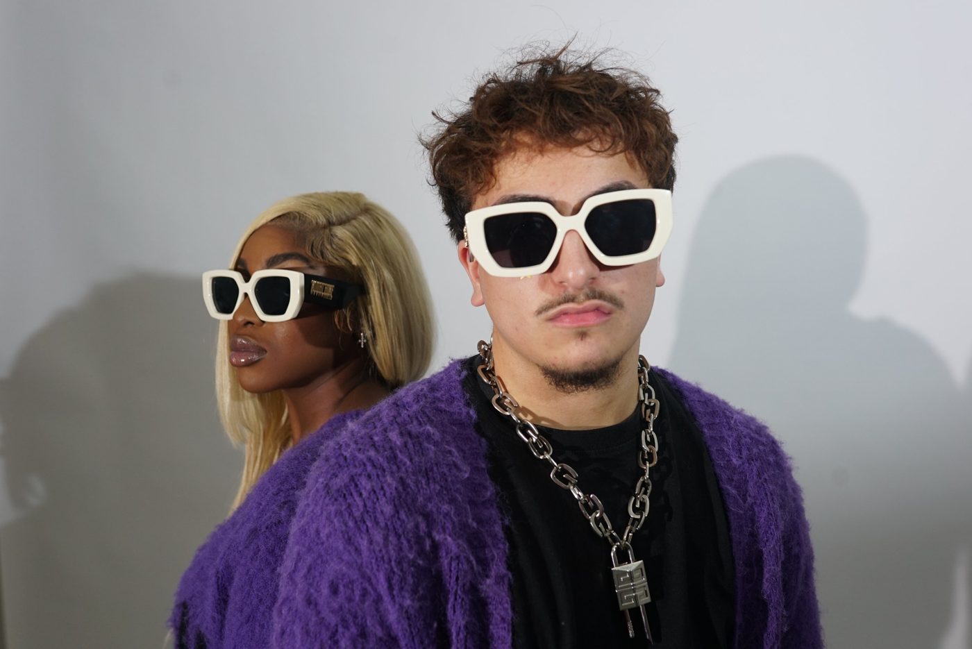Two models back to back in purple cardigans and cream statement sunglasses