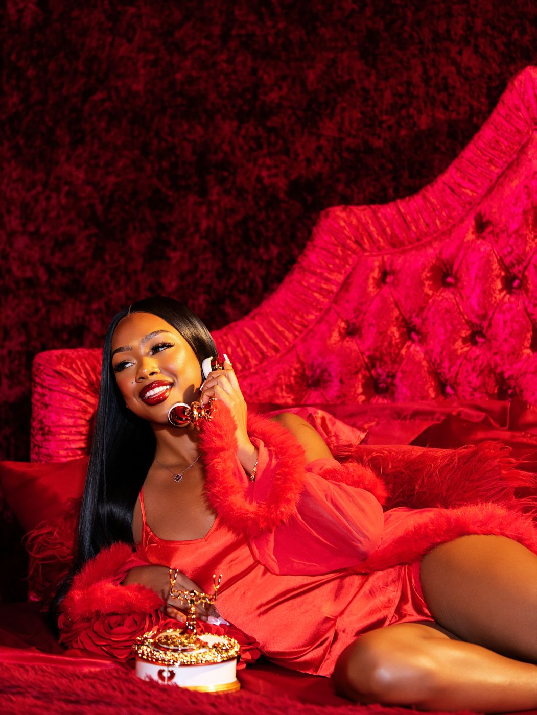 Model smiling on the gold phone in a red feather robe