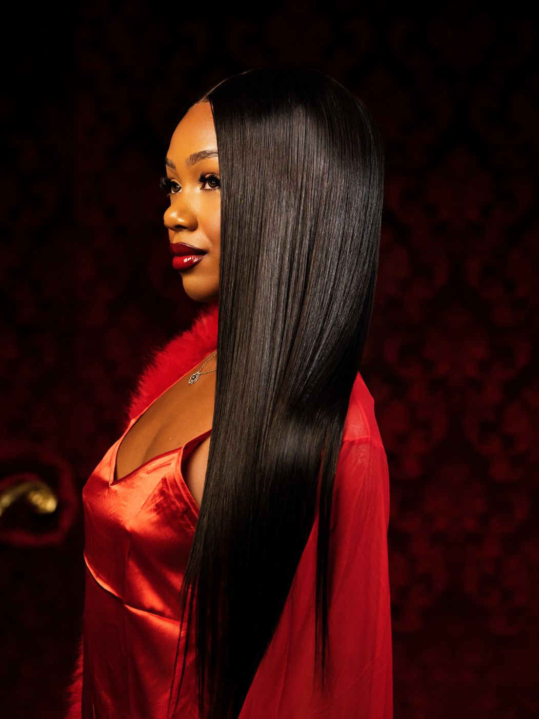 Profile portrait of the model in red satin against a dark red wall